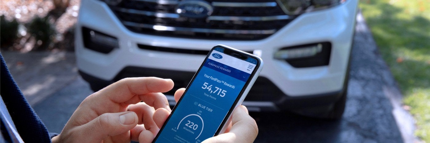Close up view of a phone displaying FordPass Rewards App with a Ford in the background